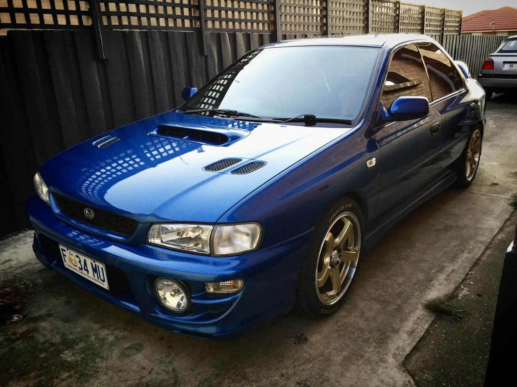 The blue Impreza WRX photographed head-on in a single-car garage, bonnet closed, under overhead light.